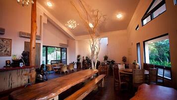 Un restaurante amplio con bancos y mesas de madera, ventanas grandes que ofrecen vistas a zonas verdes, y un candelabro colgando del techo.
