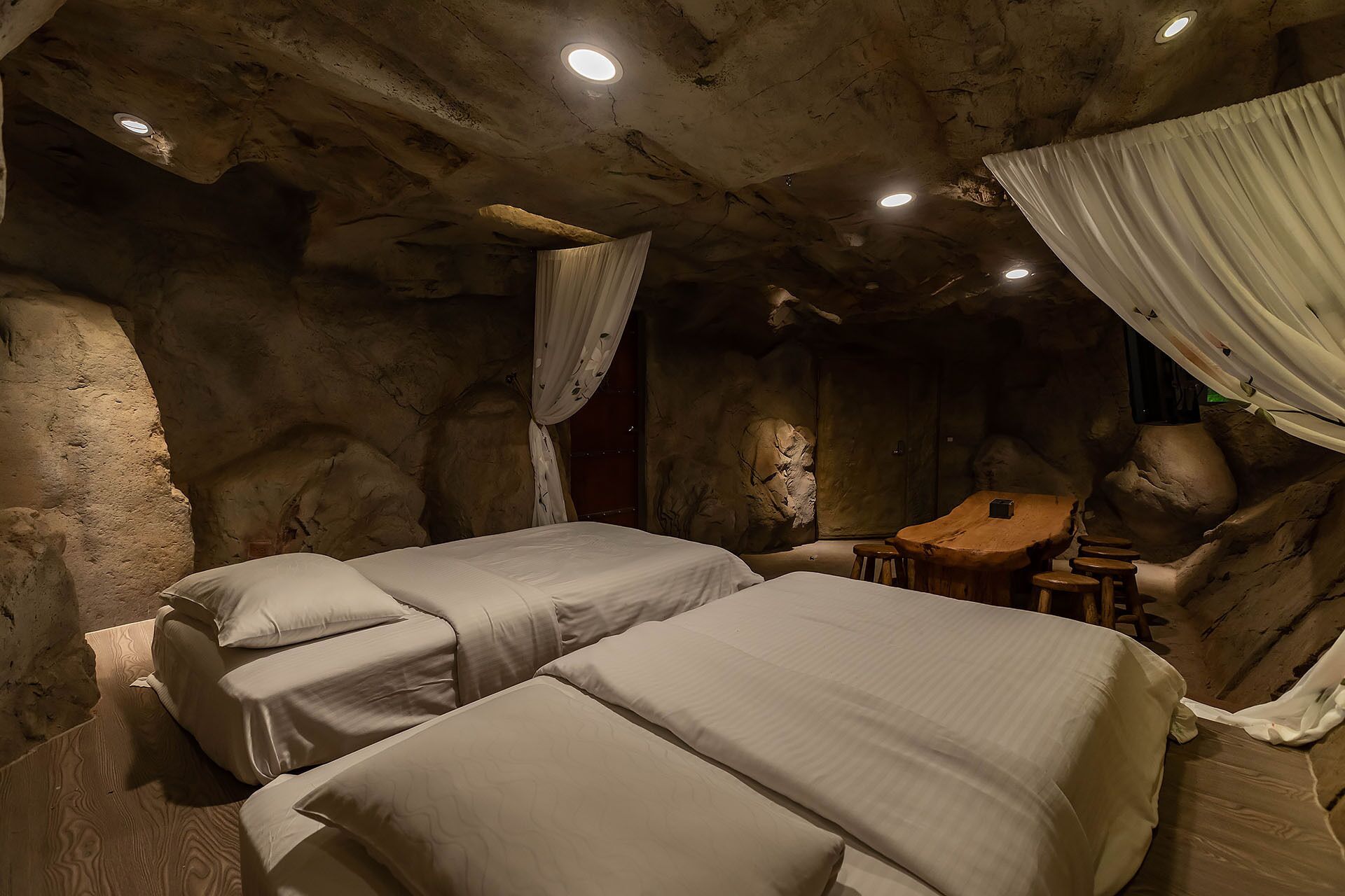 A cave-themed room with two beds, a wooden table, and a small seating area.
