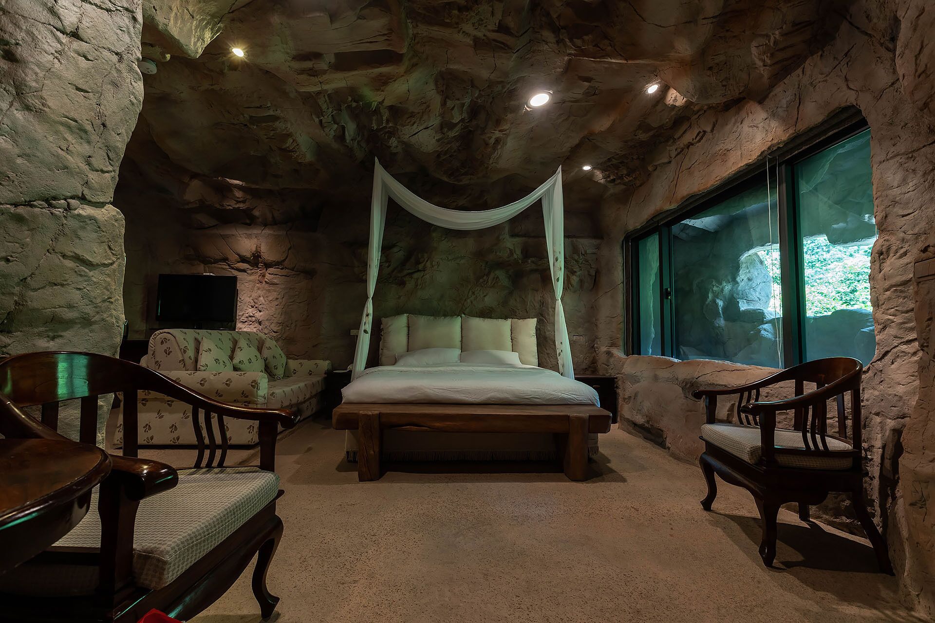 A stone-walled bedroom with a canopy bed, two wooden chairs, and a large window.