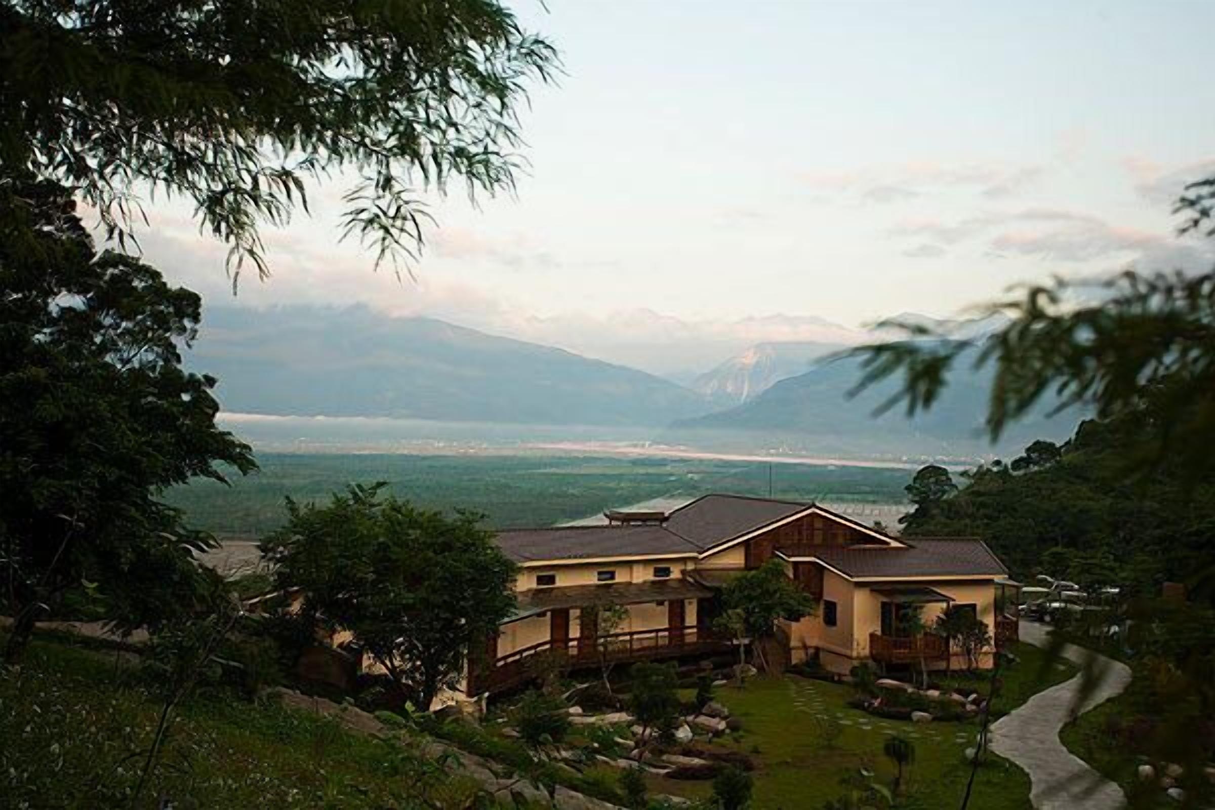 A two-story house with a large front yard, a wooden deck, and a view of mountains and a body of water.