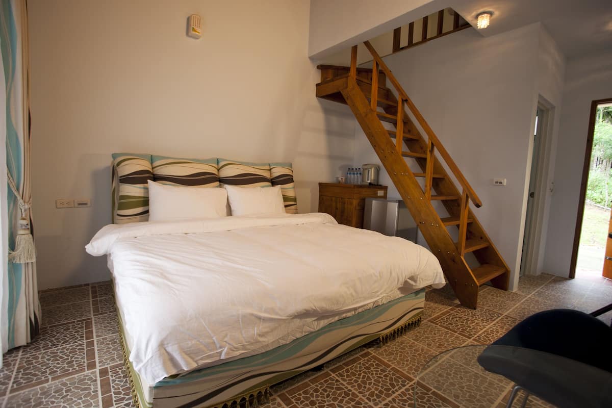 A bedroom with a large bed, a wooden staircase, and a tiled floor.