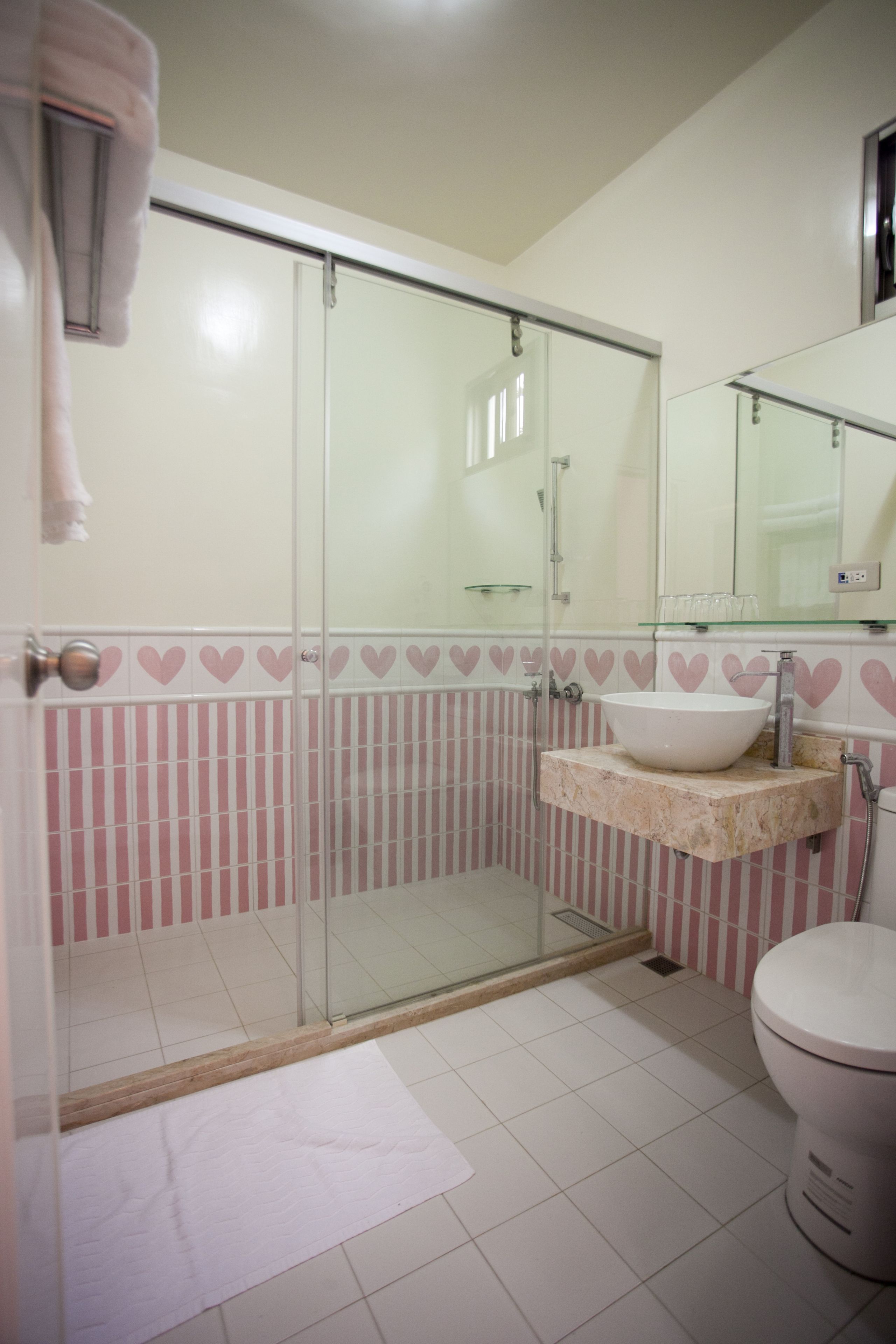 A bathroom with a glass-enclosed shower, a white sink with a marble countertop, and a toilet.