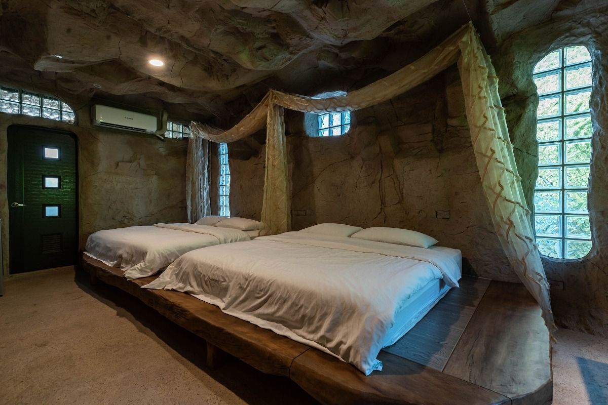 A rustic room with two beds, a bench, and large windows with curtains.