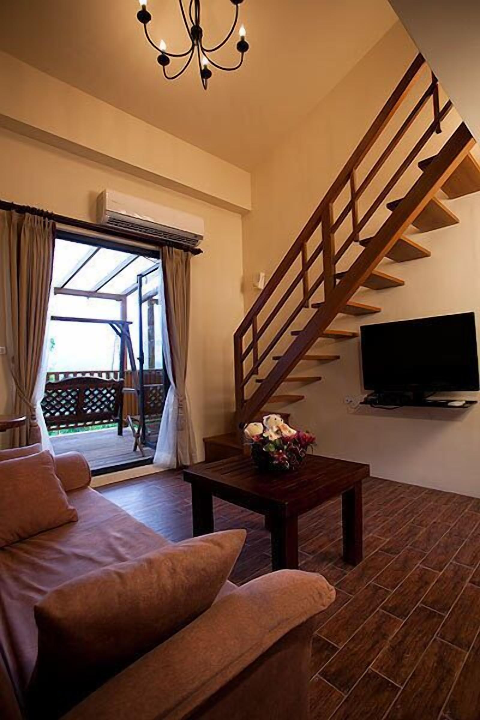 A living room with a sofa, a wooden staircase, a TV, and a view of the outdoors.
