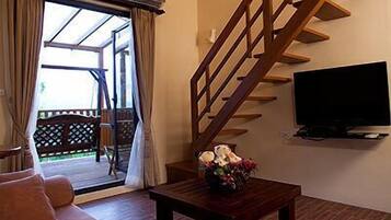 A living room with a sofa, a wooden staircase, a TV, and a view of the outdoors.