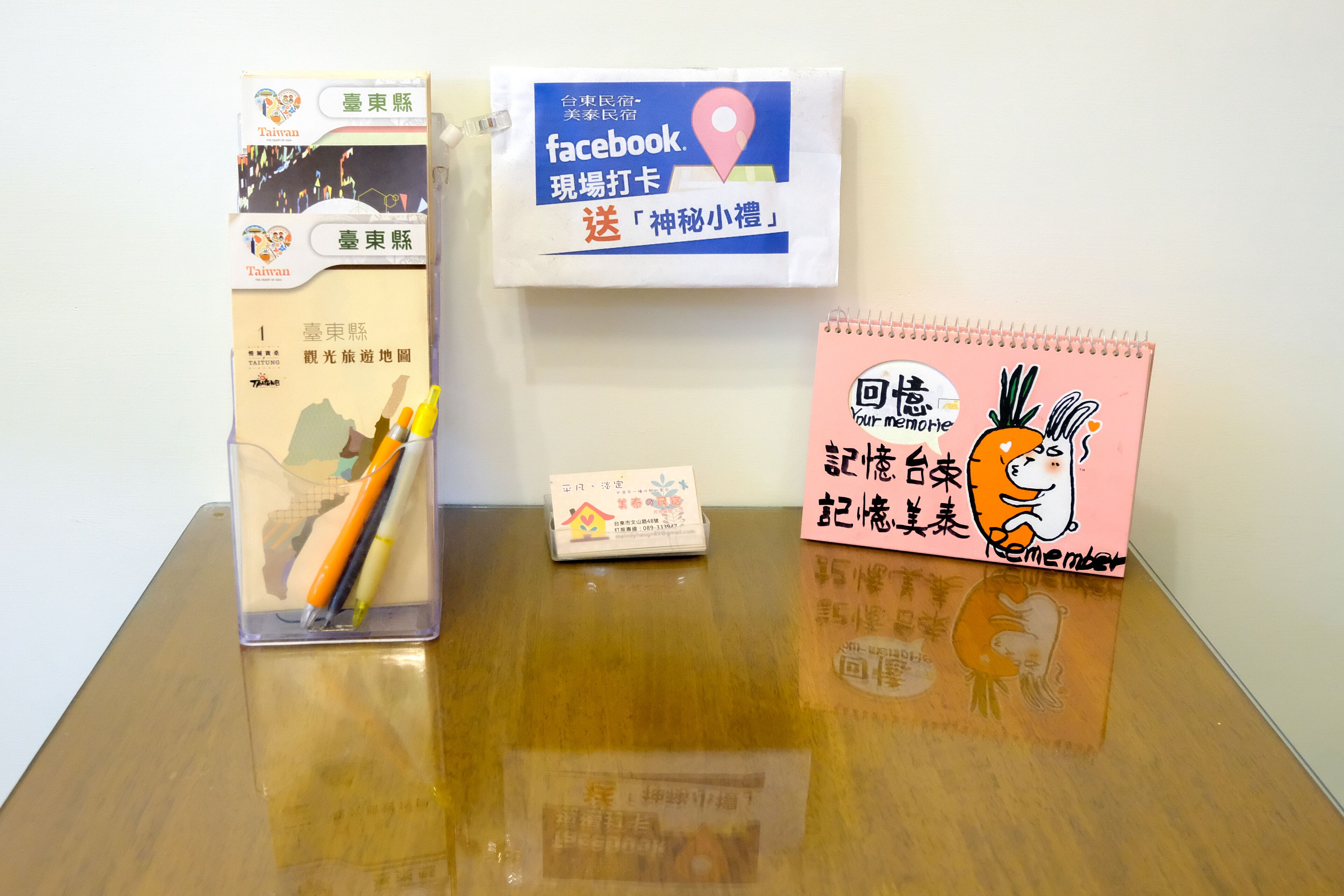 A desk with a notebook, a pen holder, a Facebook card, and a pink notepad with a cartoon character.
