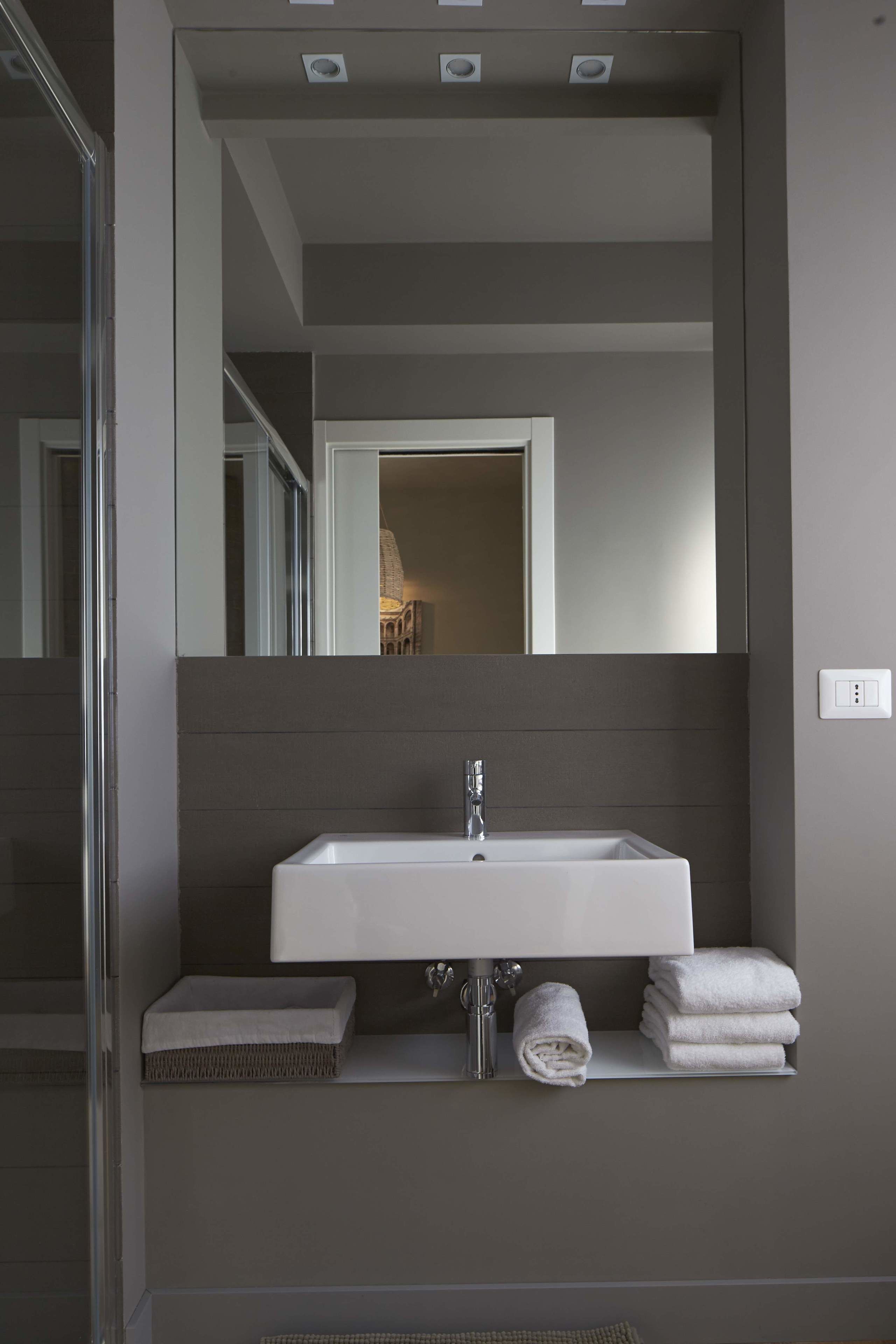A modern bathroom with a large mirror, a white sink, and a towel rack.