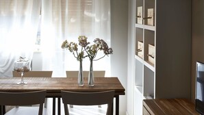 Un comedor con una mesa de madera, dos sillas, un jarrón con flores y una estantería contra la pared.