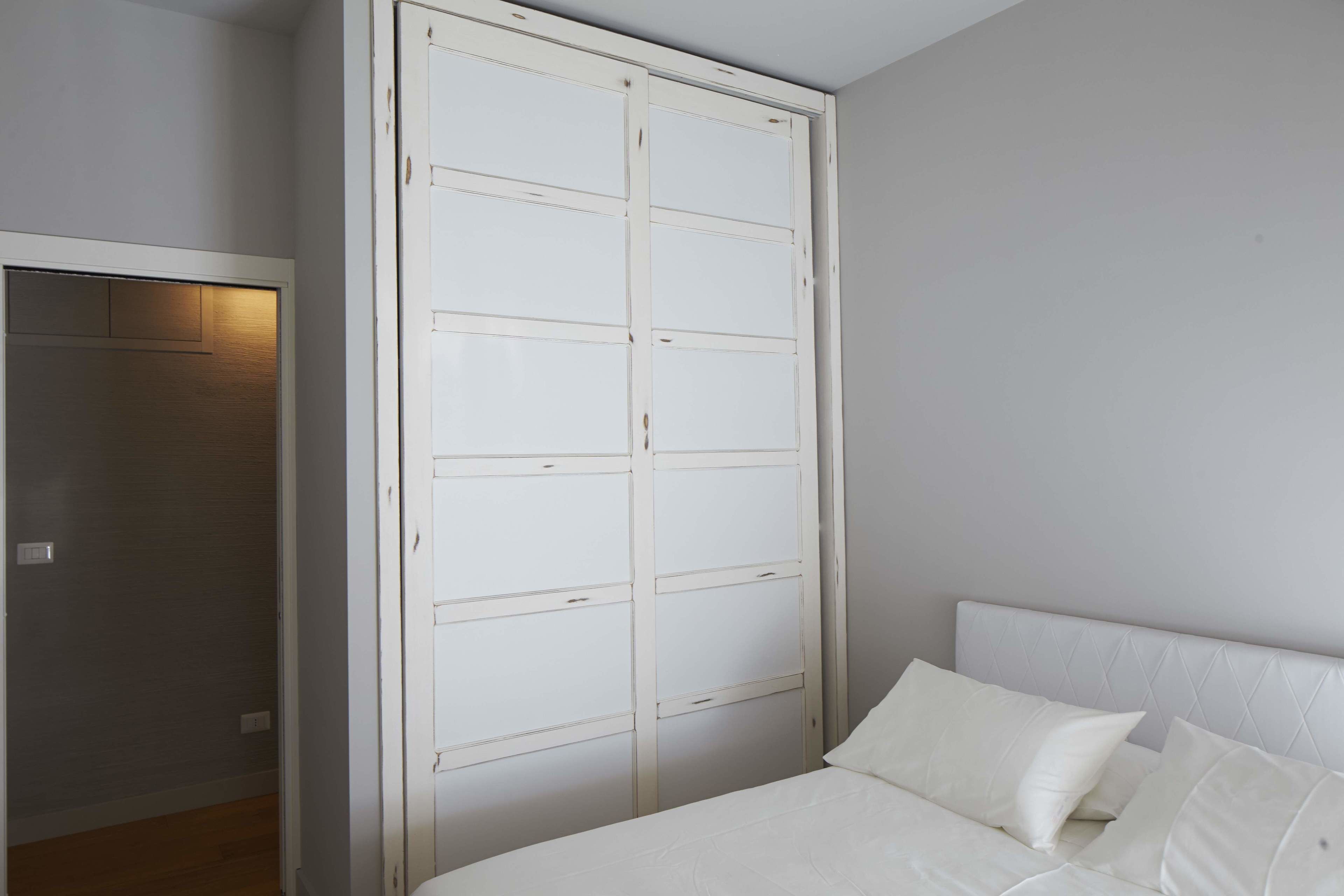 Un dormitorio con cama, cabecero blanco y un amplio armario blanco con múltiples puertas.