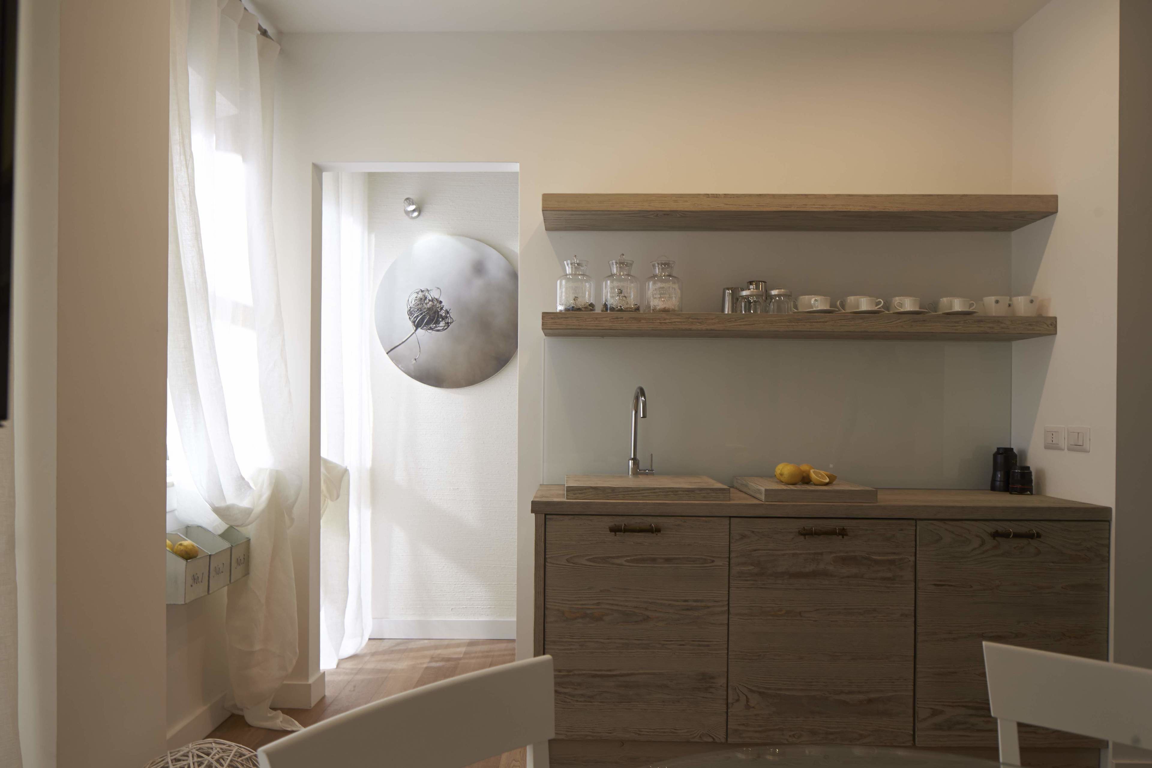 A compact kitchen with wooden cabinets, a sink, and a shelf with glass jars and cups.