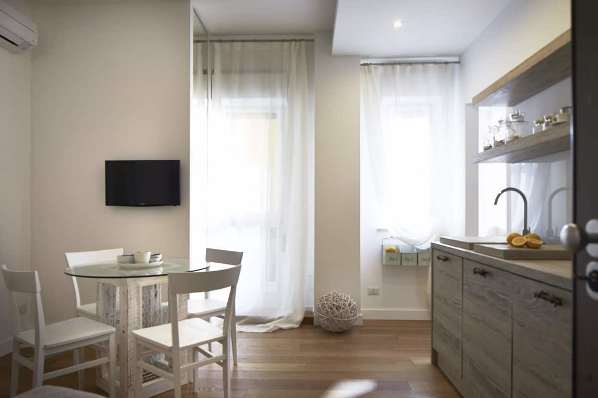 Una cocina moderna con una mesa redonda de vidrio, sillas blancas, un televisor de pantalla plana y un mueble de madera con un fregadero.