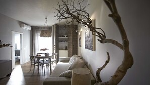 Una sala moderna con sofá, mesa de comedor y sillas. Una lámpara y una rama decorativa están en primer plano.