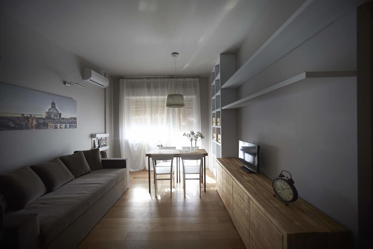 Una sala de estar moderna con un sofá, una mesa de comedor y un televisor sobre un mueble de madera.