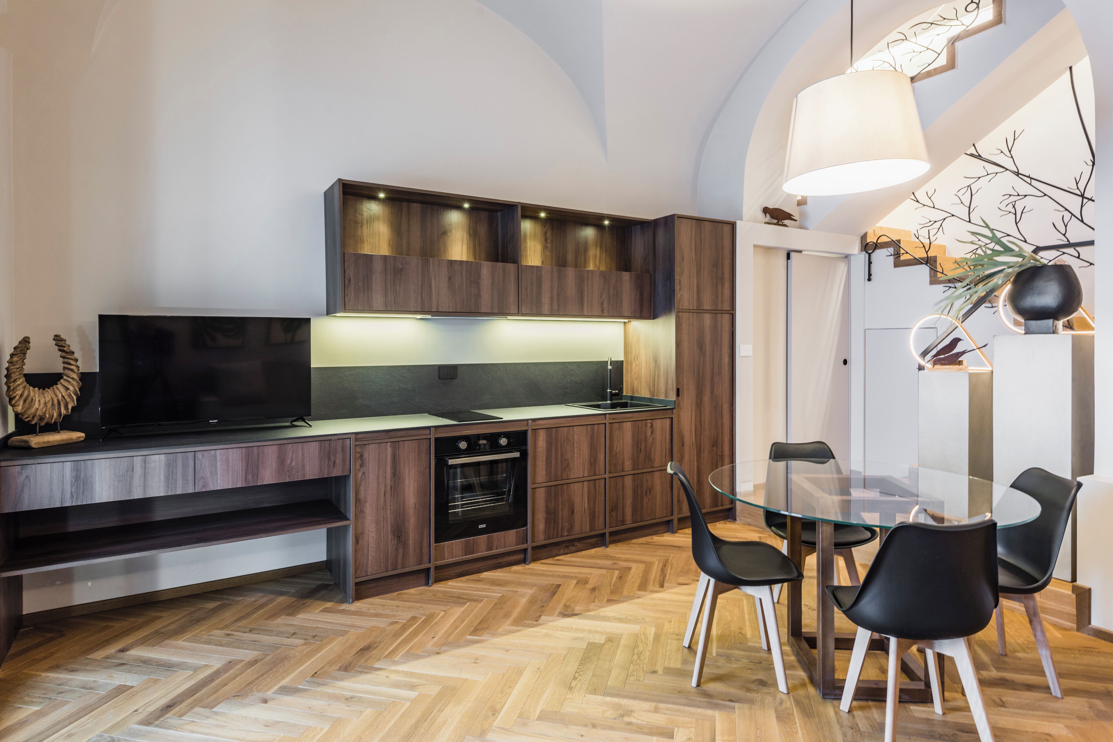 Una cocina moderna con armarios de madera, horno integrado y una mesa de comedor de vidrio con sillas negras.