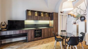 Una cocina moderna con armarios de madera, horno integrado y una mesa de comedor de vidrio con sillas negras.