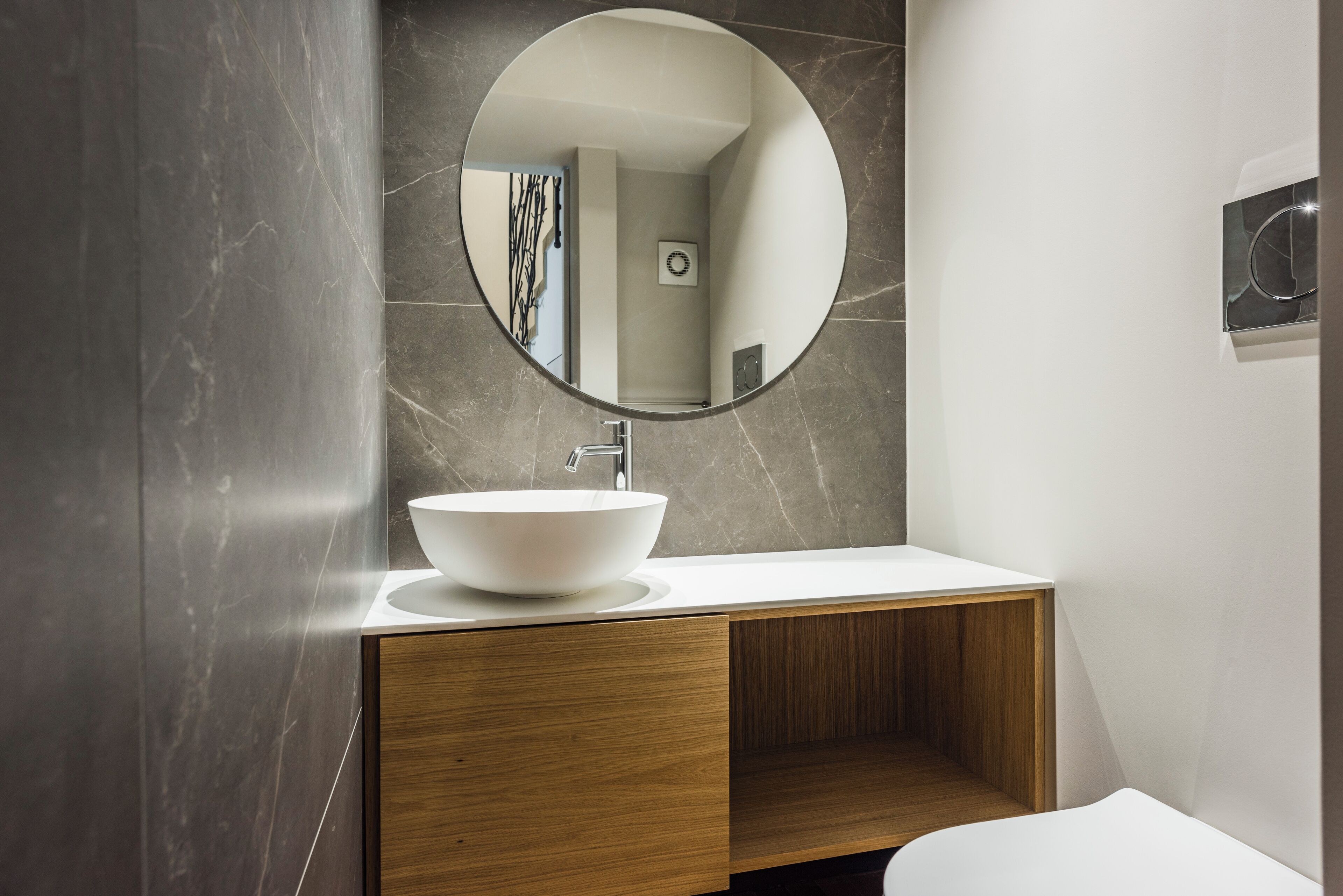 A modern bathroom with a round mirror, a white sink, and a wooden vanity.