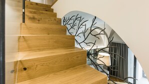 Una escalera de madera con diseño moderno que conduce a una habitación con un ventanal grande y una obra de arte original en la pared.