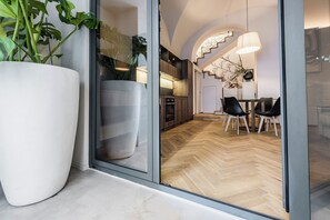 A modern interior with a large potted plant, a dining area with chairs, and a kitchen visible through a glass door. - Ferrini Home Piazza Trento (Catania)