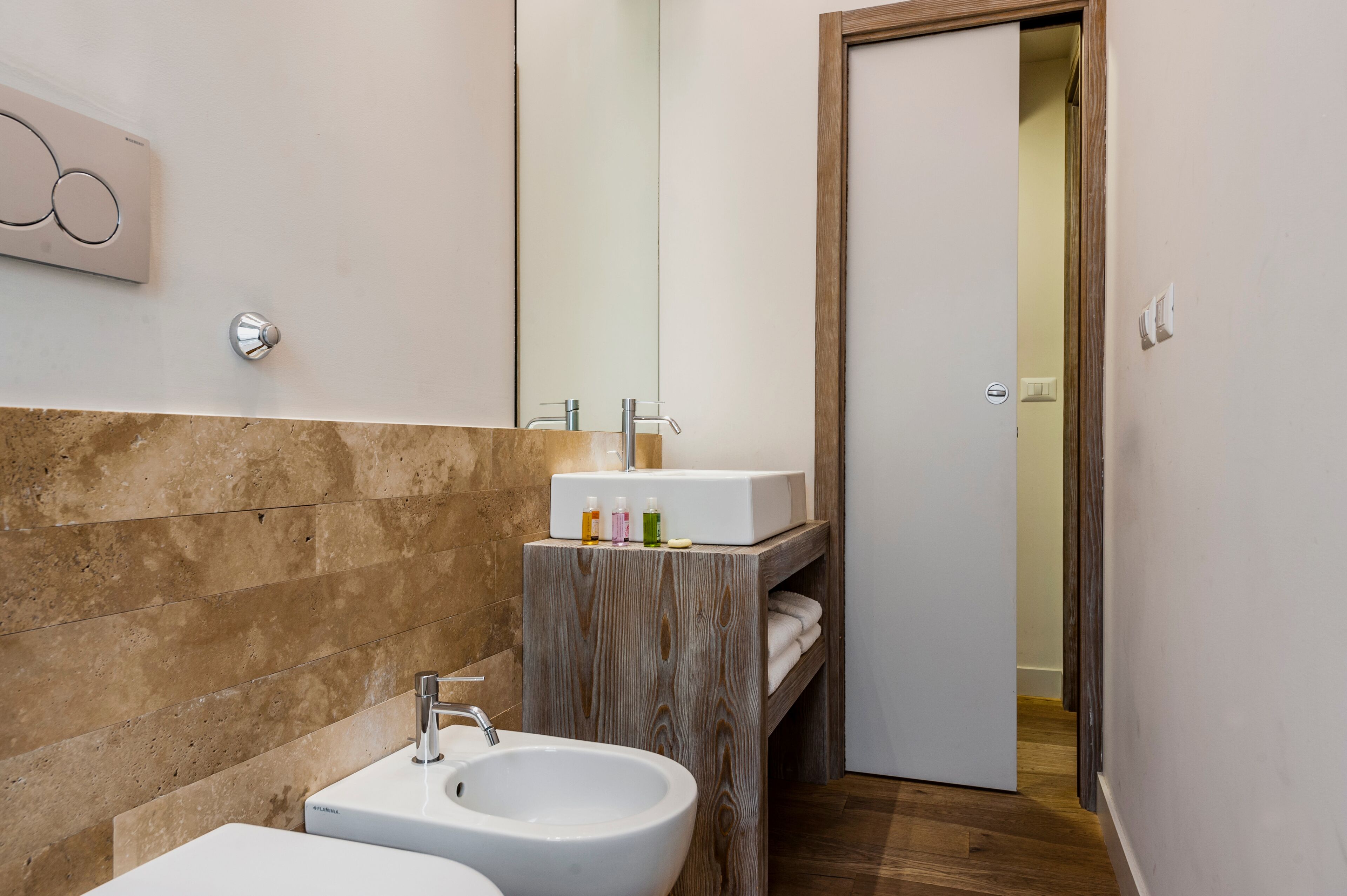 Een moderne badkamer met een marmeren wand, een houten wastafelmeubel, een wastafel en een spiegel.
