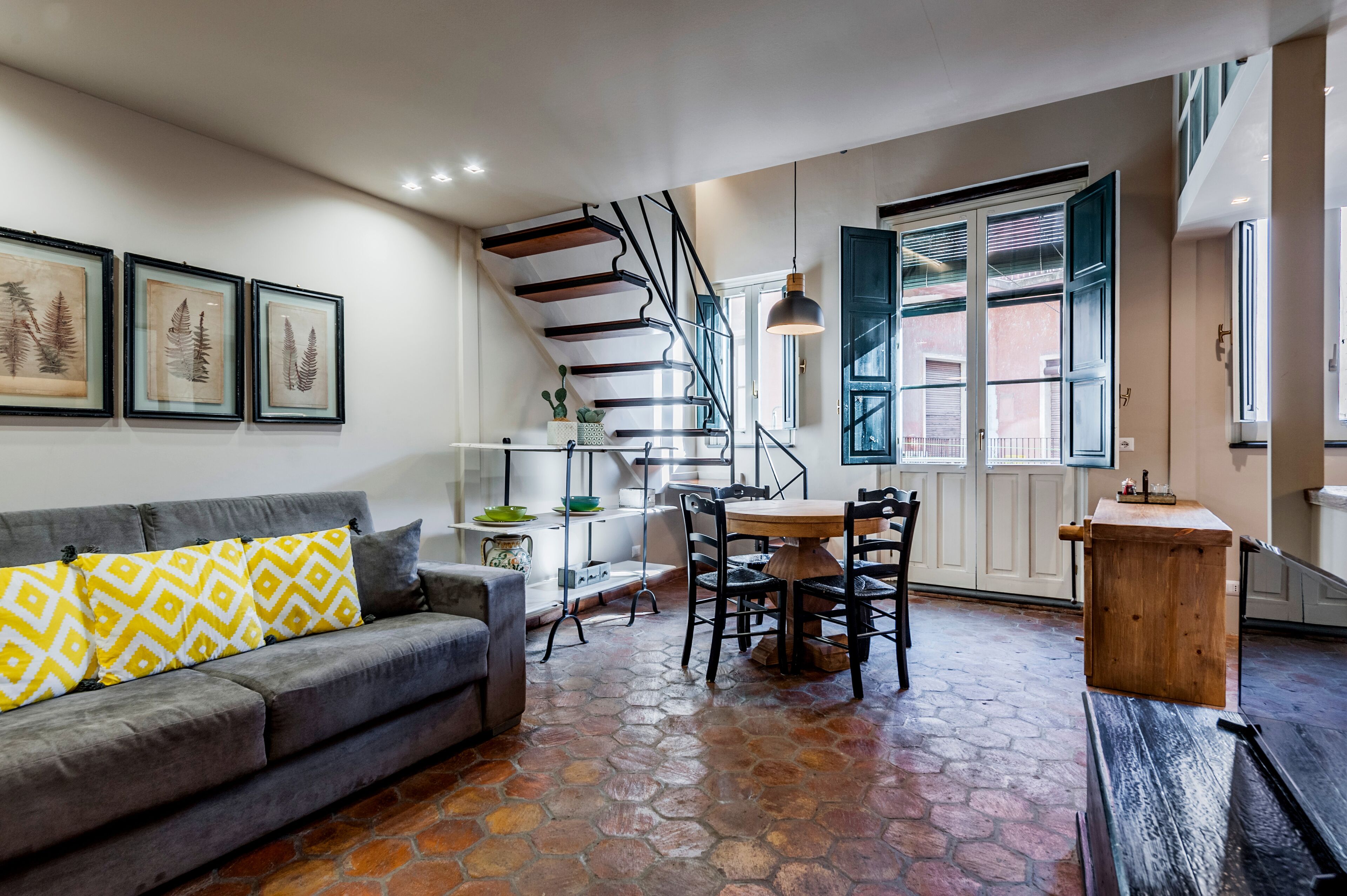 A modern living room with a gray sofa, a dining table, and a staircase.