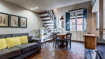 A modern living room with a gray sofa, a dining table, and a staircase.