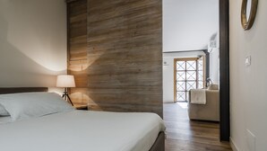 Un dormitorio con una pared de acento de madera, una cama con ropa blanca, una lámpara de noche y vistas a un baño con una toalla colgada en la puerta.