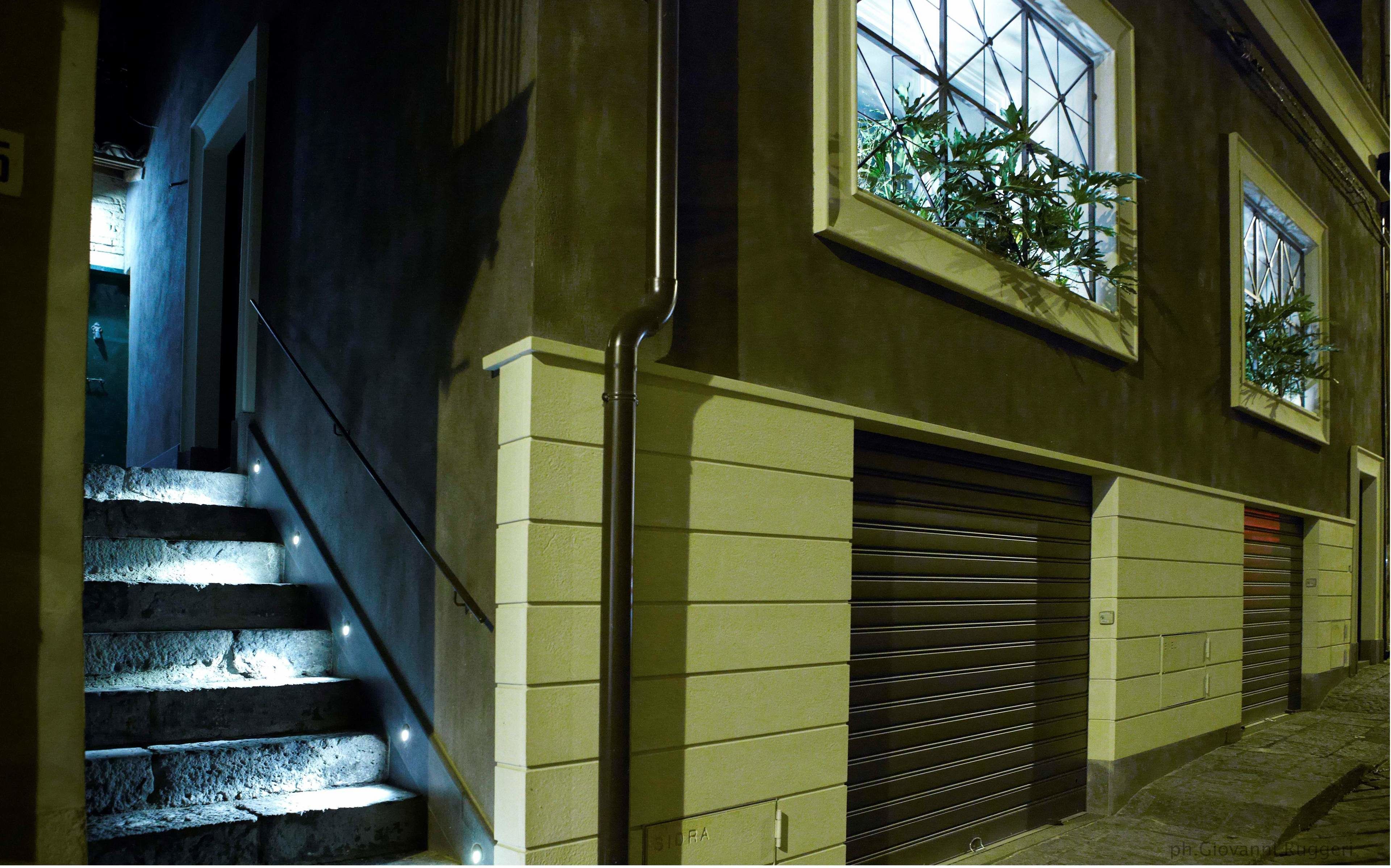 Un edificio con una escalera que lleva a una plataforma, una puerta de garaje cerrada y una ventana con una planta.
