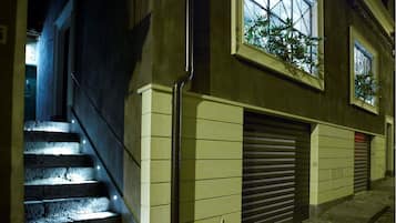 Un edificio con una escalera que lleva a una plataforma, una puerta de garaje cerrada y una ventana con una planta.