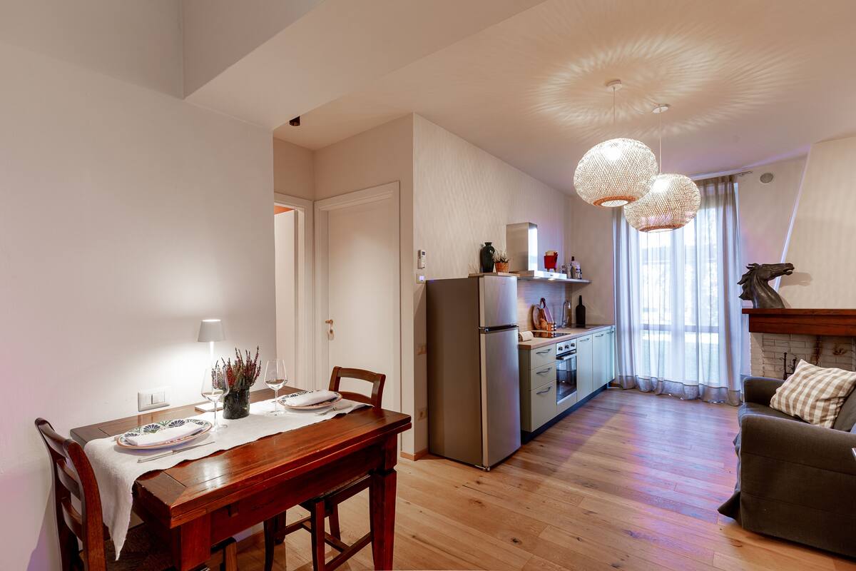Una cocina moderna con horno y refrigerador integrados, un comedor con mesa y sillas de madera, y una sala de estar con sofá y chimenea.