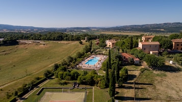 A large outdoor swimming pool surrounded by lush greenery and a tennis court.