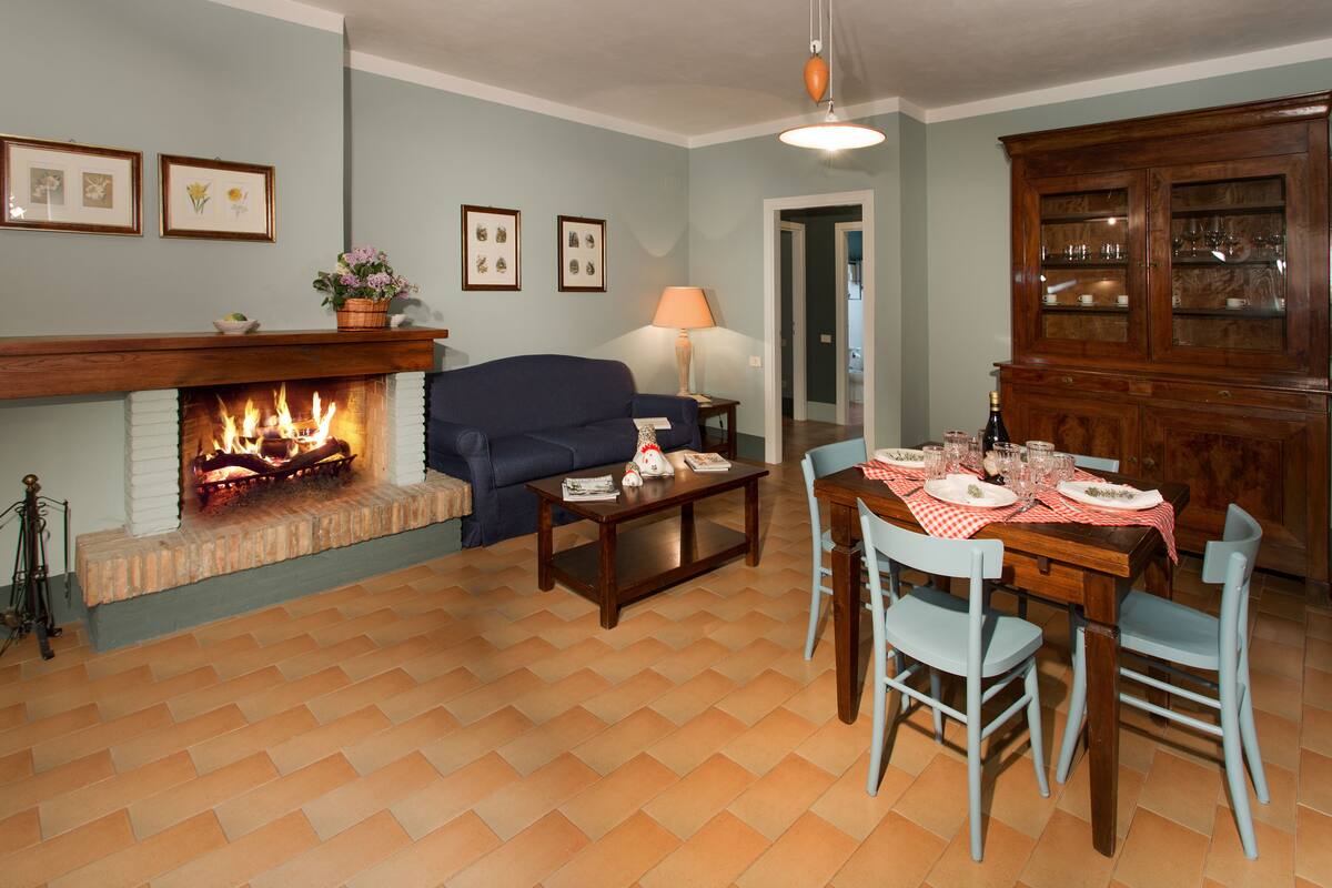 Una sala de estar con chimenea, un sofá, una mesa de comedor para cuatro personas y un aparador de madera.