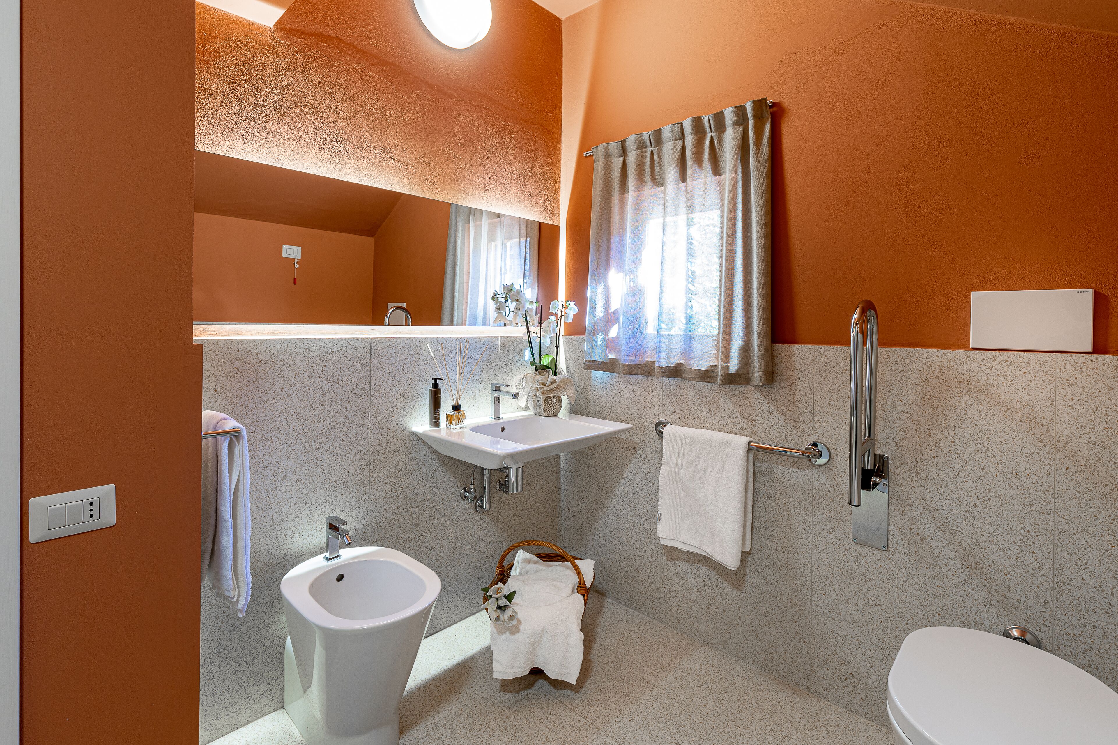 A bathroom with a sink, bidet, and toilet, a towel rack, and a mirror.