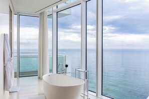 A modern bathroom with a freestanding bathtub, large windows, and a view of the ocean. - SEAMARQ Hotel (Gangneung)