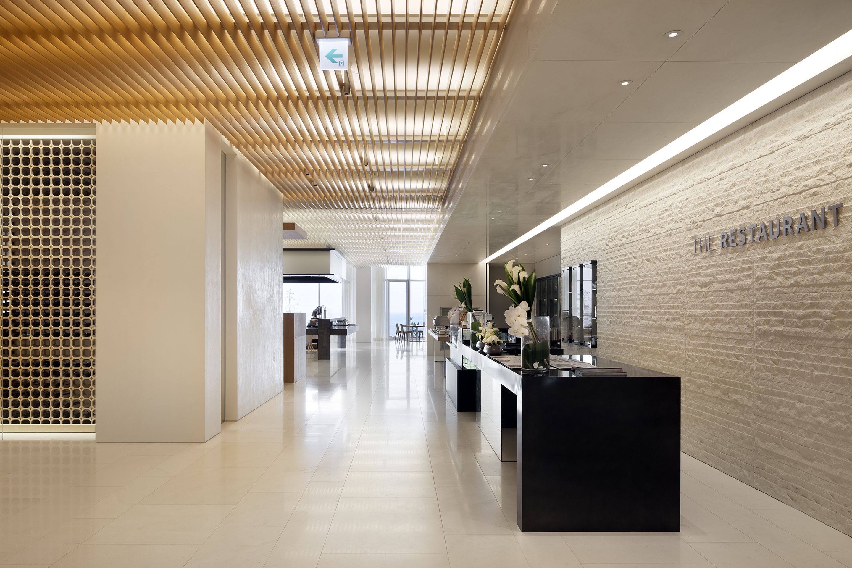 Un espace d’accueil moderne avec un plafond en bois, un comptoir d’accueil et un mur sur lequel est inscrit le texte : « LE RESTAURANT ».