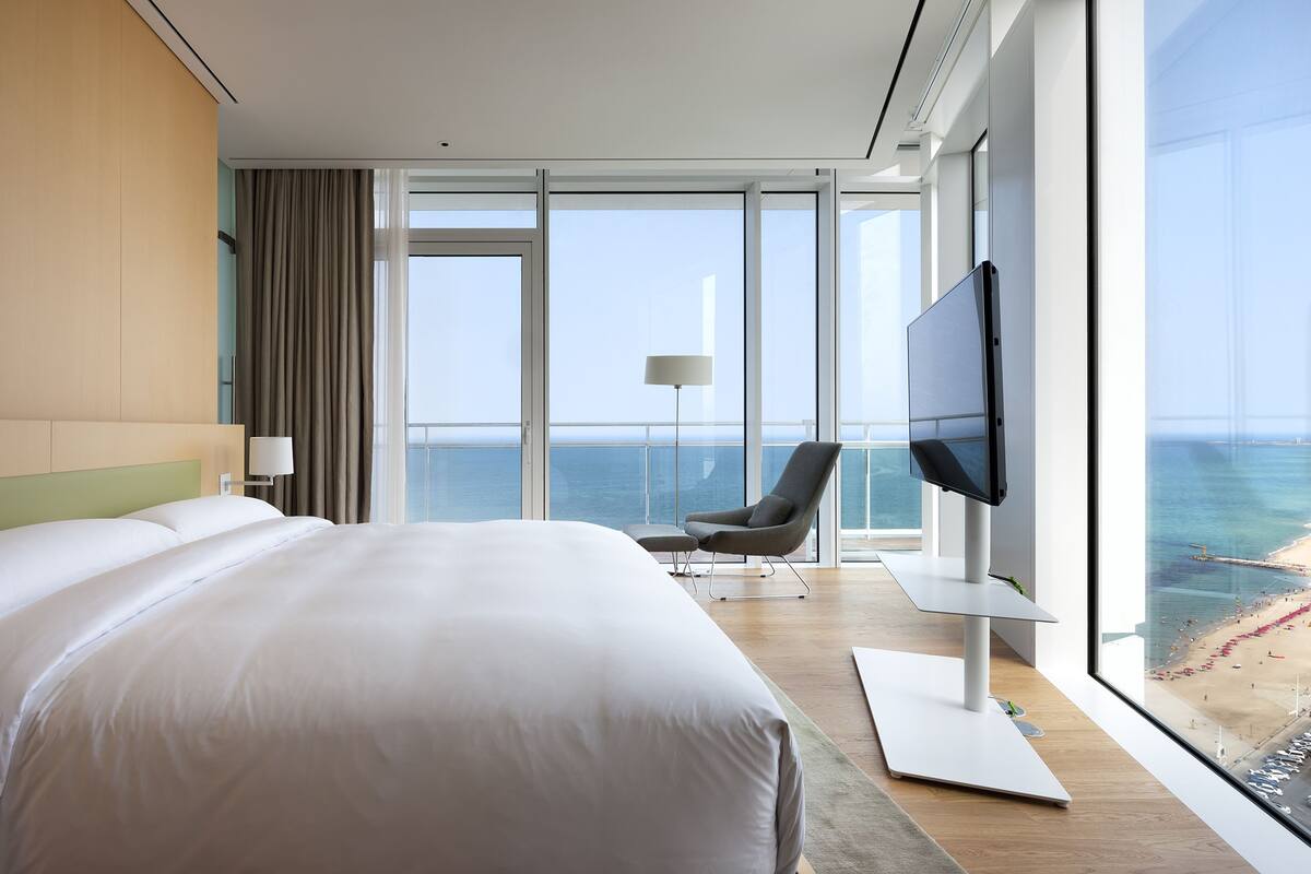 Quarto de hotel moderno com uma cama grande, uma televisão e vista para o mar.