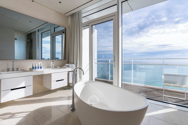 A modern bathroom with a freestanding bathtub, a large mirror, and a view of the sea. - SEAMARQ Hotel (Gangneung)