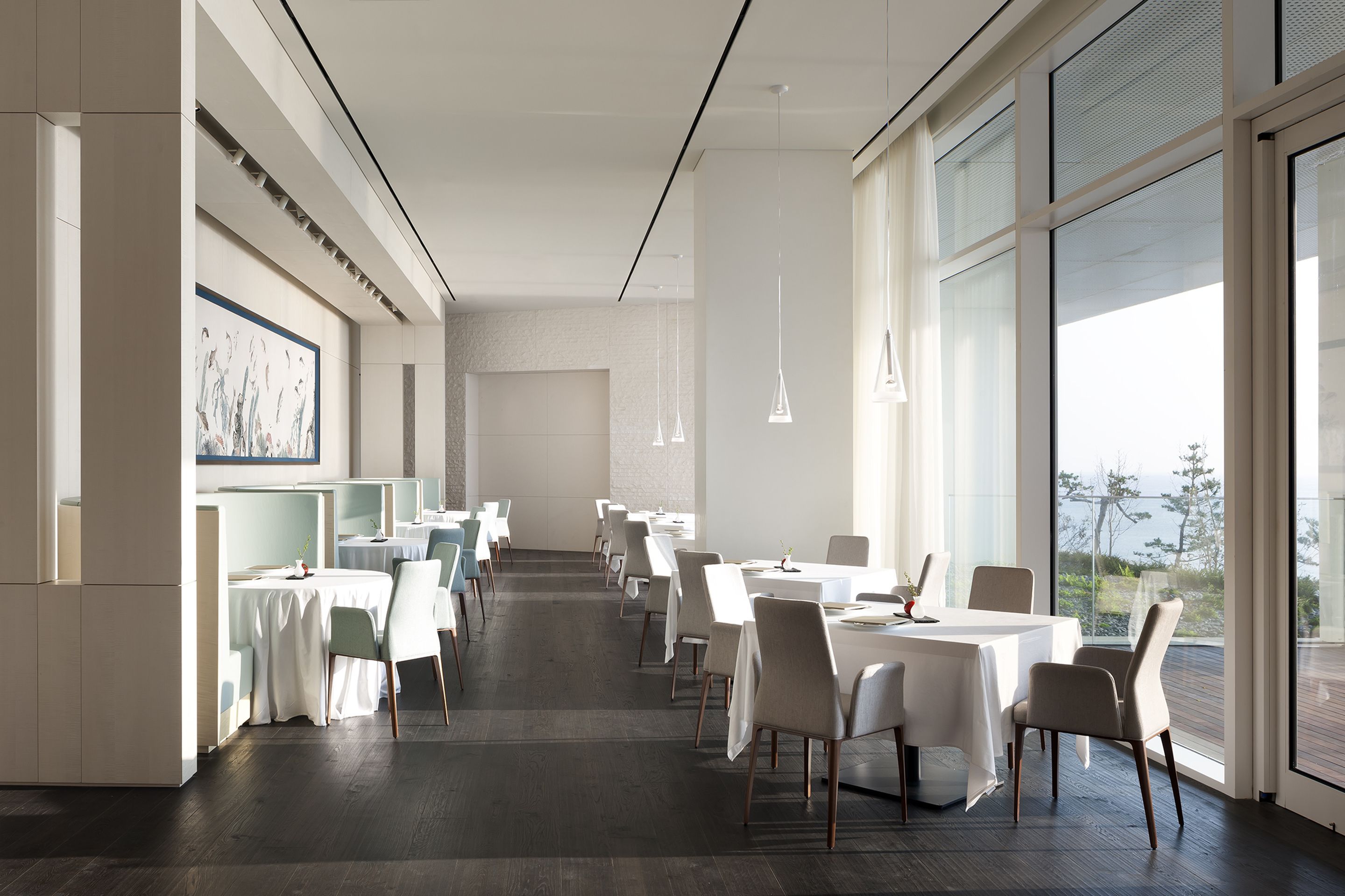 Un espace de restauration moderne avec des tables et des chaises blanches, de grandes fenêtres et des luminaires suspendus.