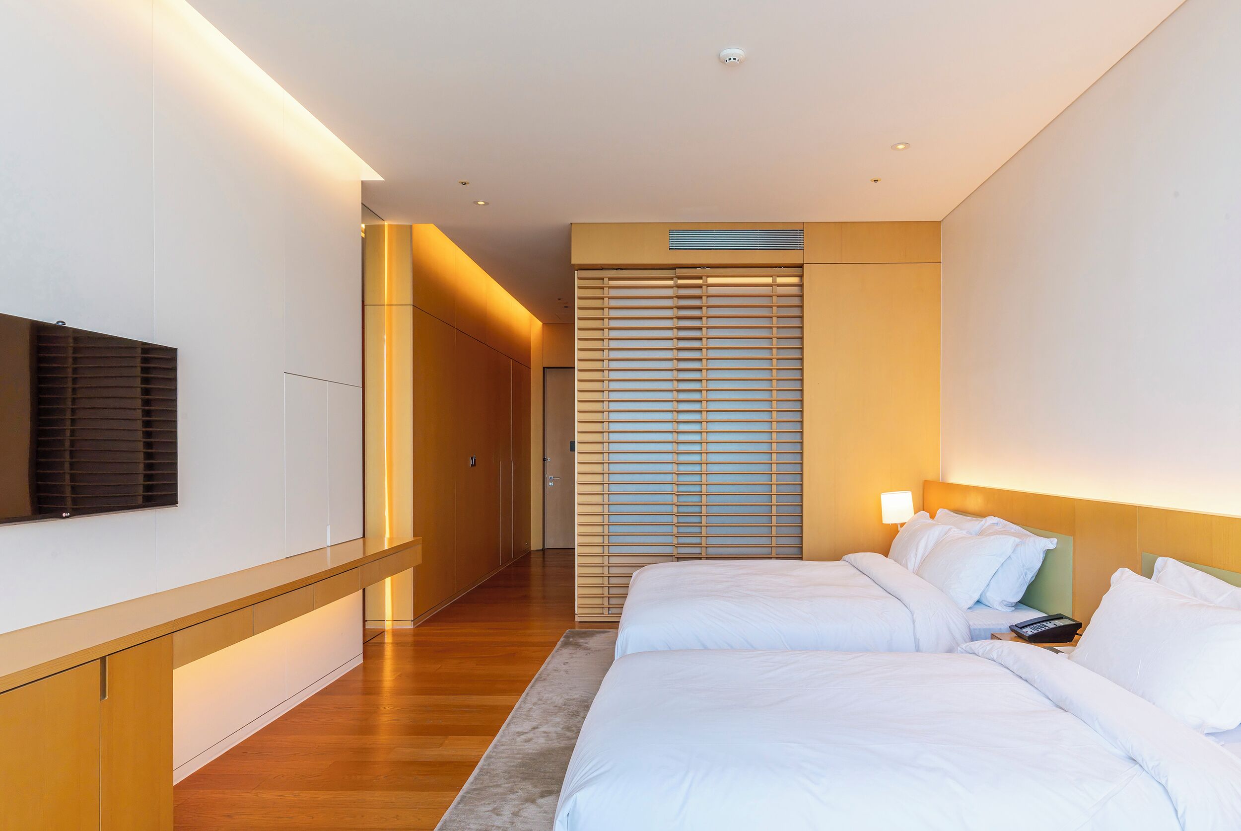 A hotel room with a bed, bedside table, lamp, and a TV mounted on the wall.