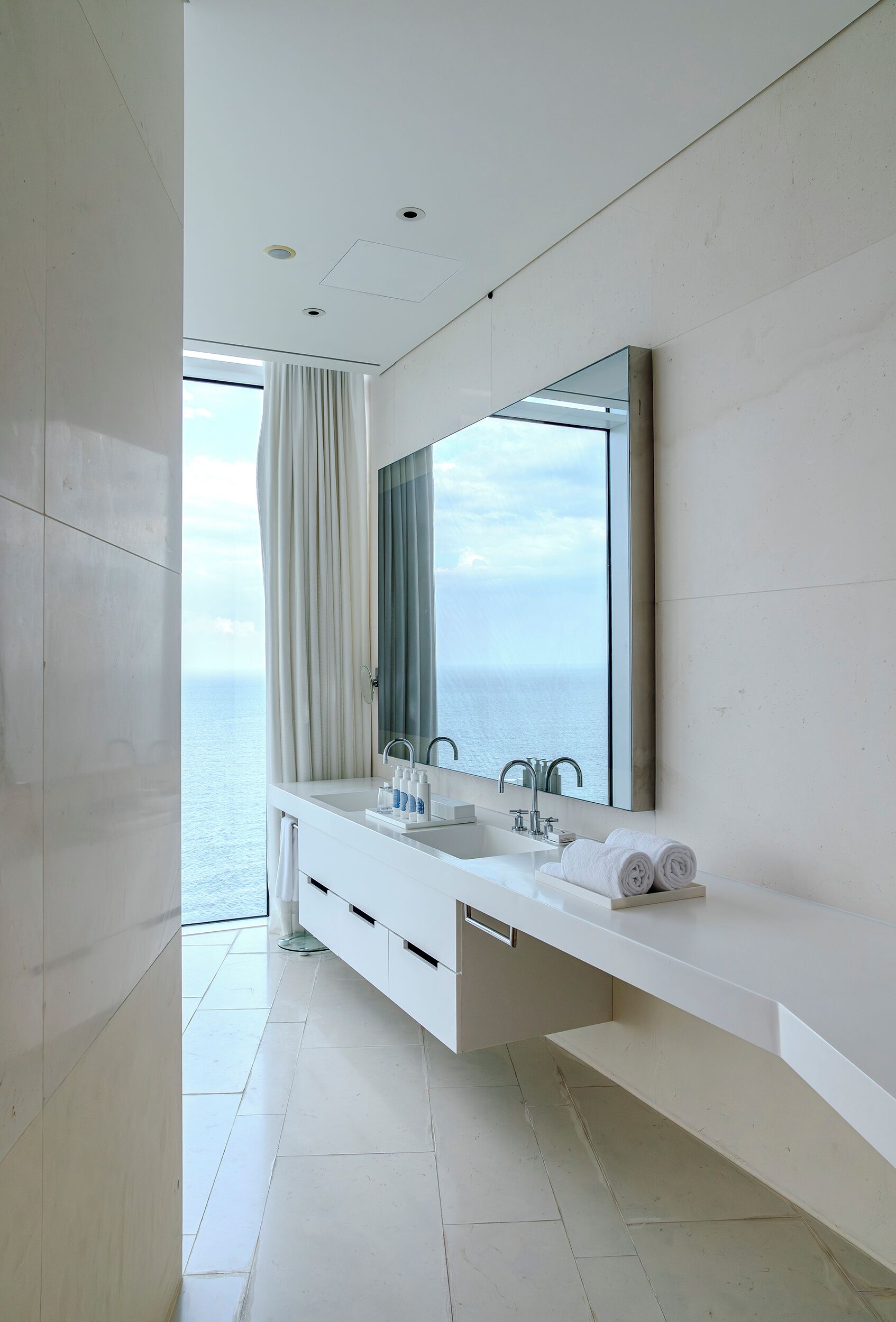 Un baño moderno con un espejo grande, dos lavamanos y vistas al mar.