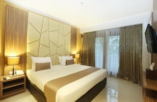 A hotel room with a large bed, a flat-screen TV, a bedside table with a lamp, and a window with curtains.