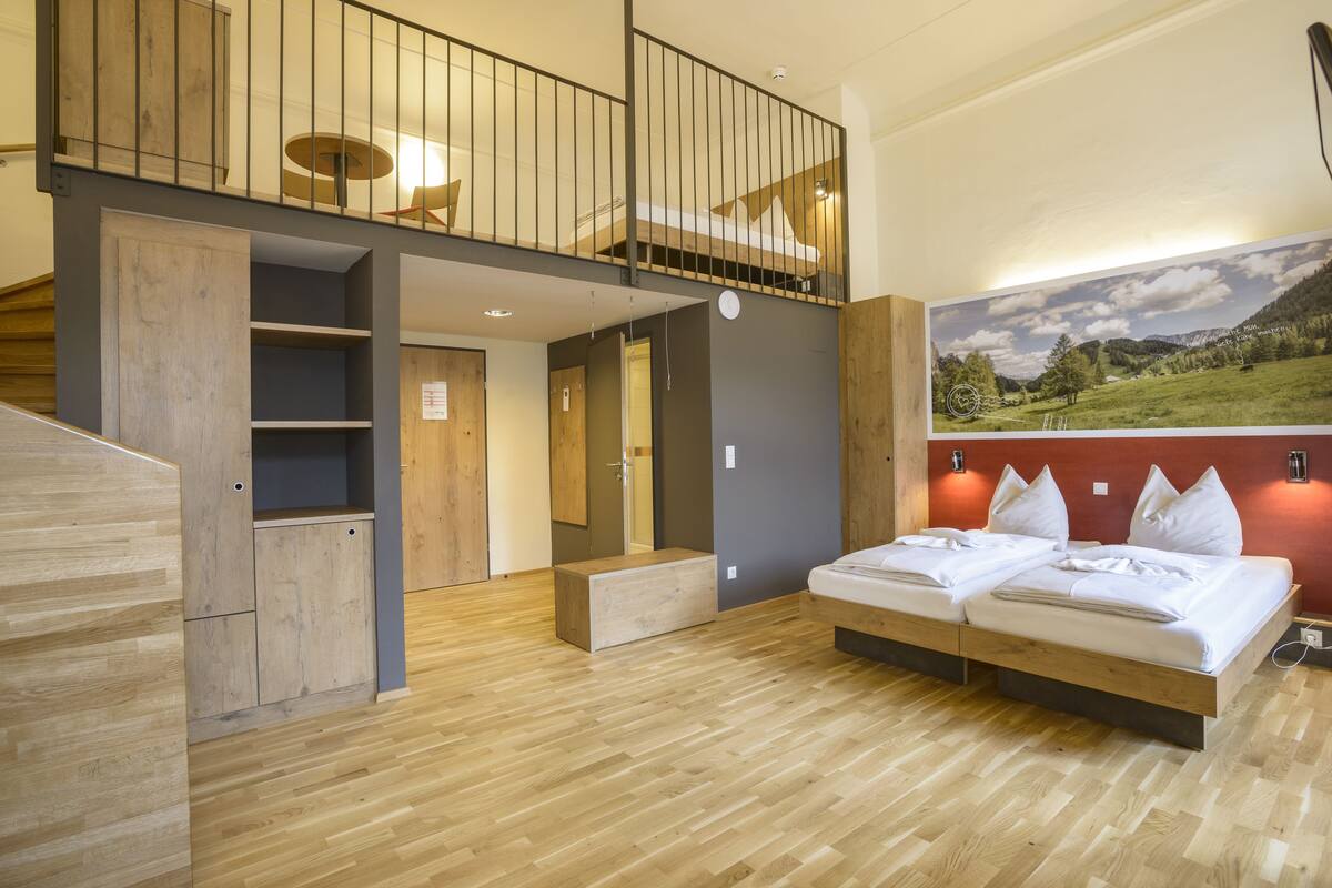 Una habitación moderna con cama estilo altillo, piso de madera y un cuadro de paisaje grande en la pared.