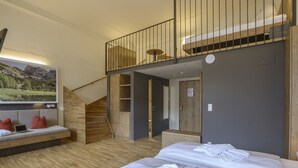 A modern hotel room with a wooden staircase, a bed with white linens, a seating area with a laptop, and a large landscape painting.
