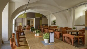 A spacious dining area with long wooden tables and chairs, potted plants, and a menu stand.