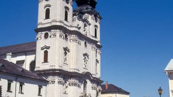 Una iglesia histórica con dos torres principales y un campanario central, rodeada de una zona pavimentada con plantas florecientes.