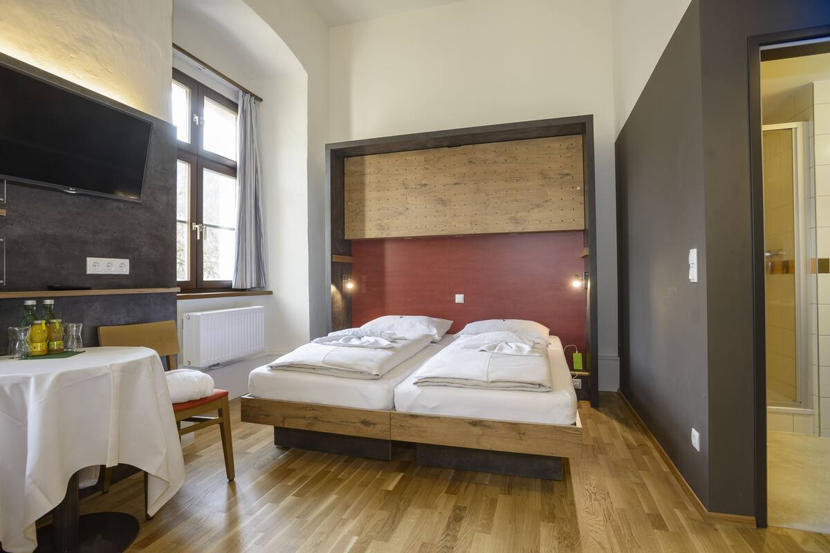 Un dormitorio con dos camas, una mesa con mantel blanco y un televisor montado en la pared.