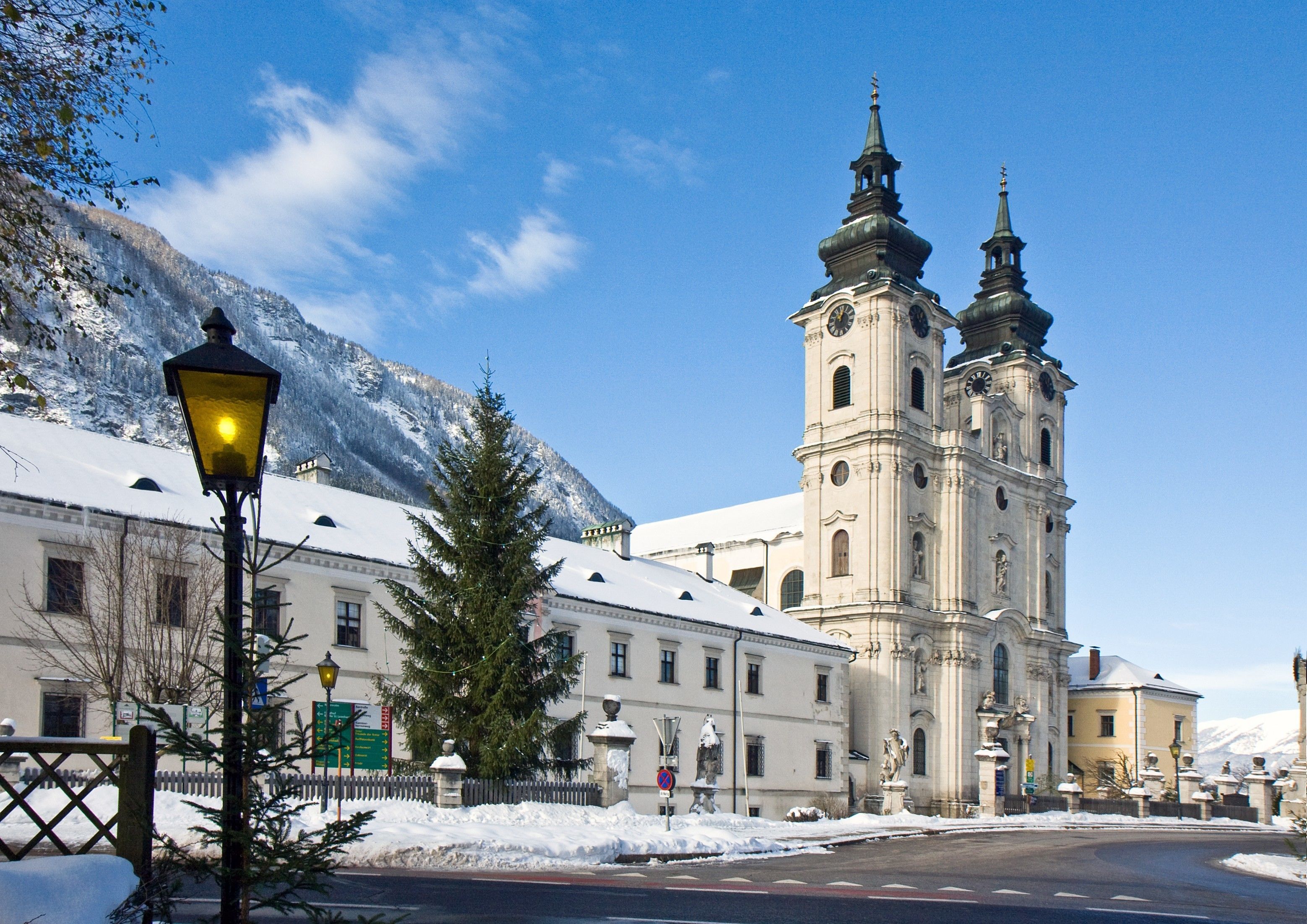 Ein historisches Gebäude mit einem markanten Glockenturm, umgeben von schneebedeckten Bergen und einem klaren Himmel.