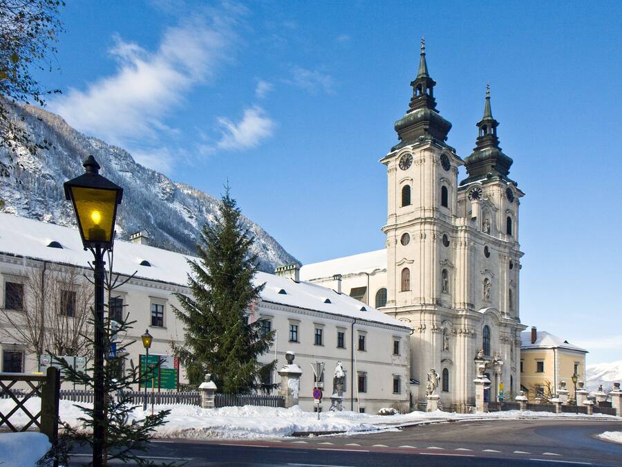 Ein historisches Gebäude mit einem markanten Glockenturm, umgeben von schneebedeckten Bergen und einem klaren Himmel.