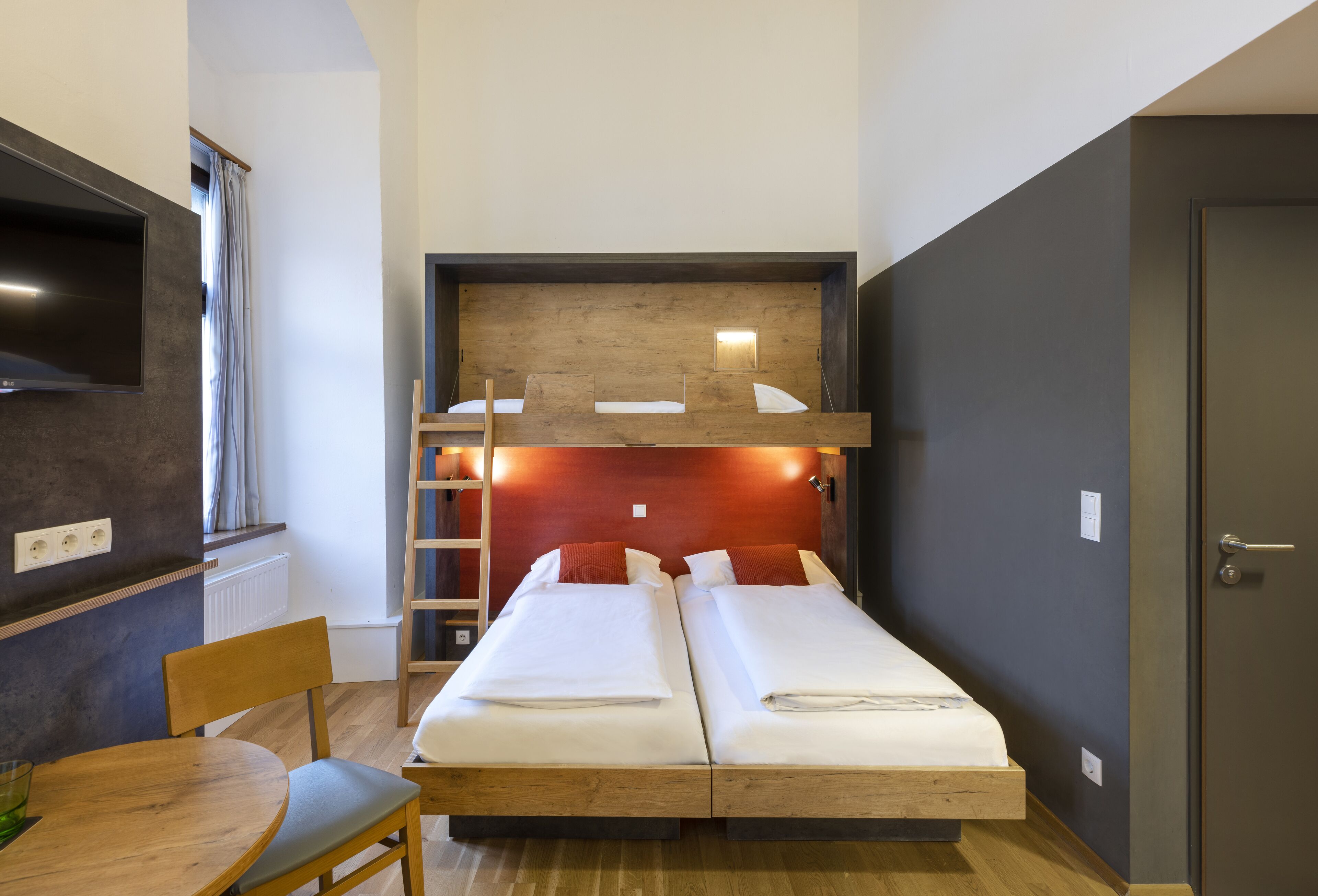 Une petite pièce comprenant un lit superposé, une petite table et une chaise.