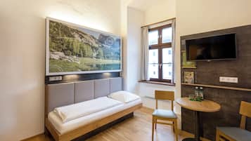 A modern room with a bed, a TV mounted on the wall, a window with curtains, and a small table with chairs.