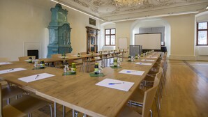 A conference room with long tables, chairs, a chandelier, and a large clock.